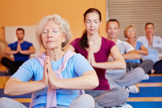 Seated yoga participants with hands folded and eyes closed.